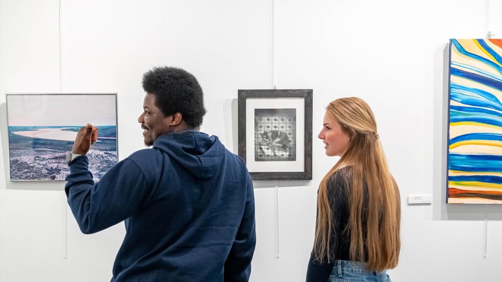 Two St. Scholastica students look at the art hanging in the student center.