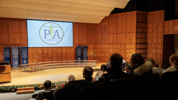 PA Medicine graduation in Mitchell Auditorium. St. Scholastica PA Medicine logo appears on a screen.