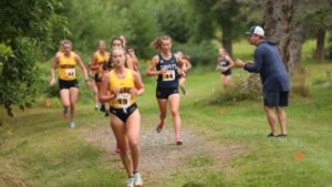 Female cross country runner runs on a grassy field.