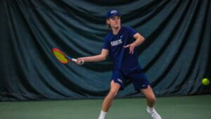 Male tennis player swings at tennis ball.