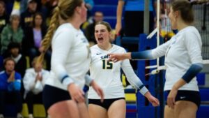 Three volleyball players cheering near the volleyball net.