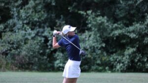 Female golf player swinging at a golf ball.