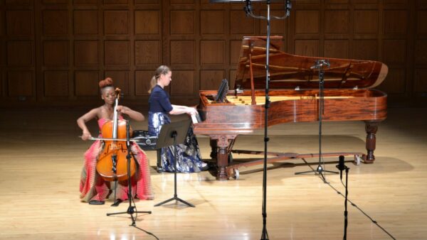 Ifetayo Ali-Landing plays the cello on the stage of Mitchell Auditorium. A piano accompanist plays behind Ali-Landing.