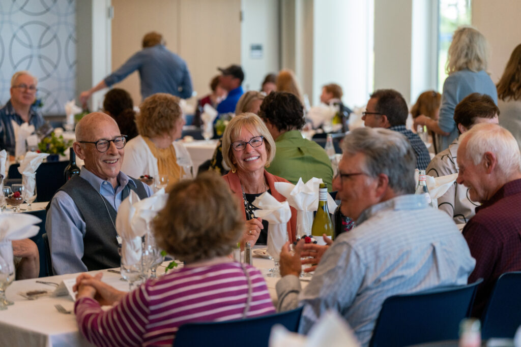 Attendees of a dinner smile in conversation with one another