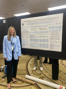 Gracie Meagher smiles in front of her research poster at a conference.