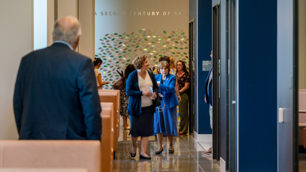 A group tours the new Student Center. Behind the group, there is a feature wall with art for the A Second Century of Saints campaign.