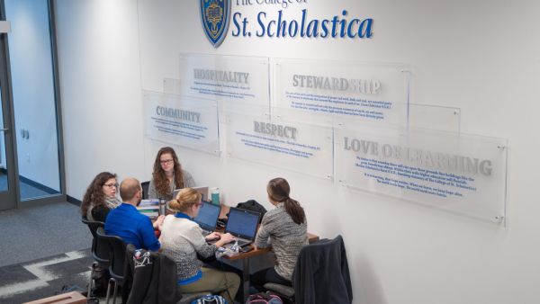 Five students study at a table in the Health Science Center. On the wall above the table is a display of the five values of St. Scholastica: hospitality, stewardship, community, respect and love of learning.