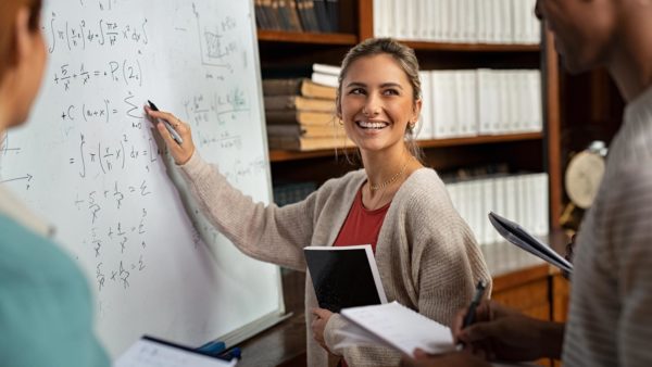 Mathematics student working through a formula on a white board.