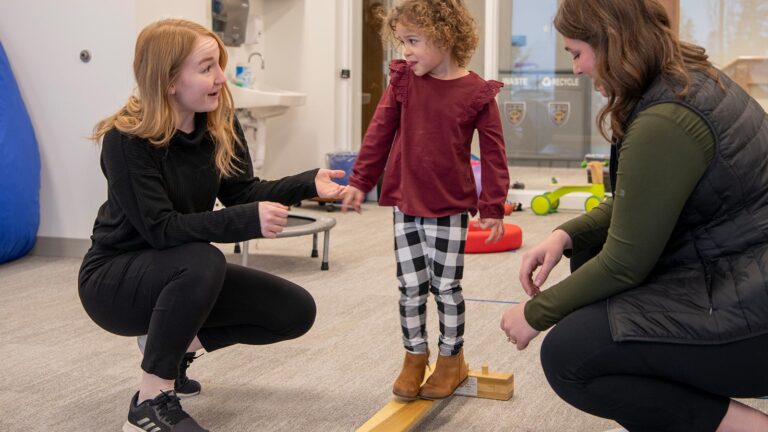 Occupational therapist works with a child on a balance beam at the Maurice's Community Clinic.