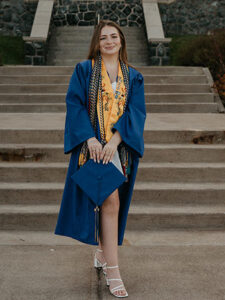 Portrait of Renee Booth in front of Tower Hall in her graduation gown