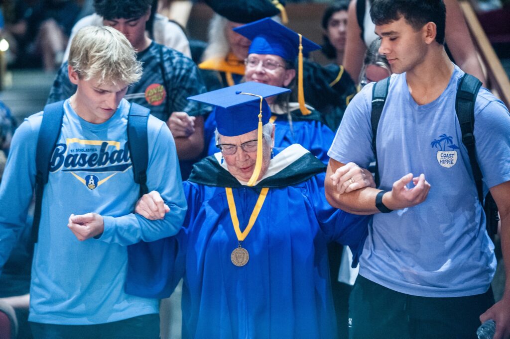 Students assist alumni going down the stairs of Mitchell Auditorium.