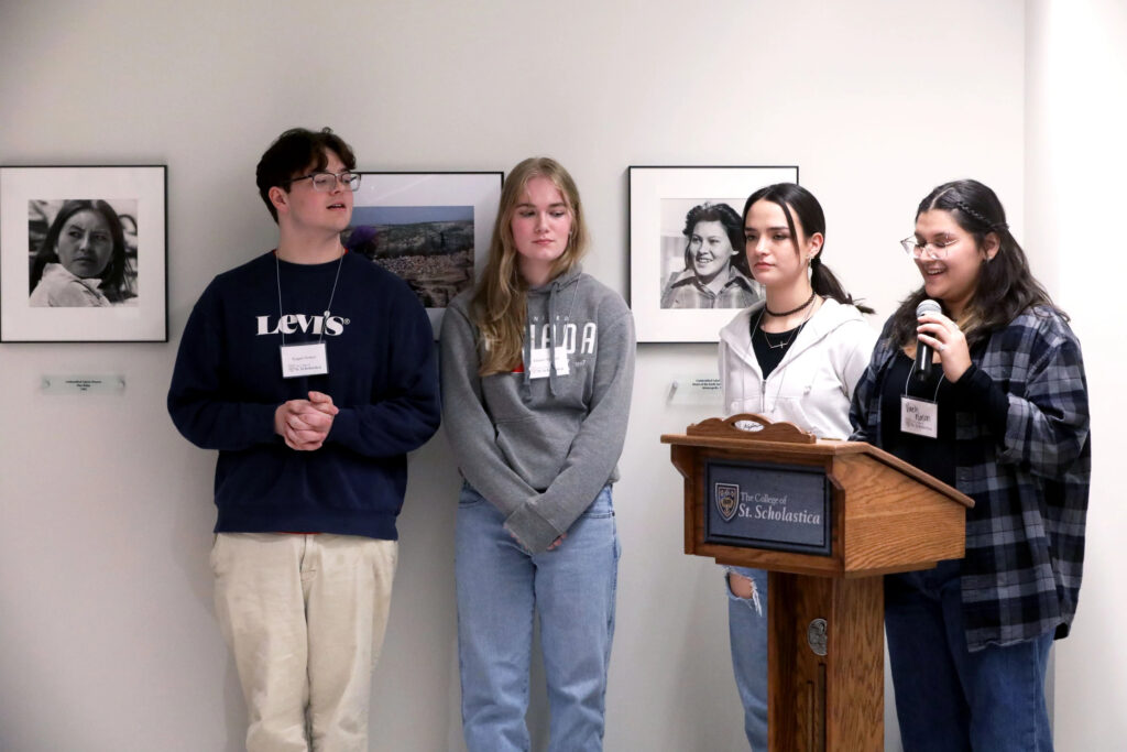 Four students near a podium at the AIM Exhibit.