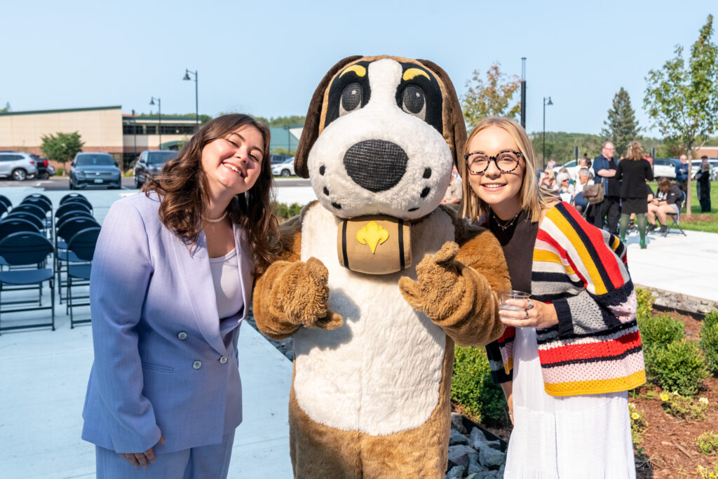 Two students smile with Storm the mascot.