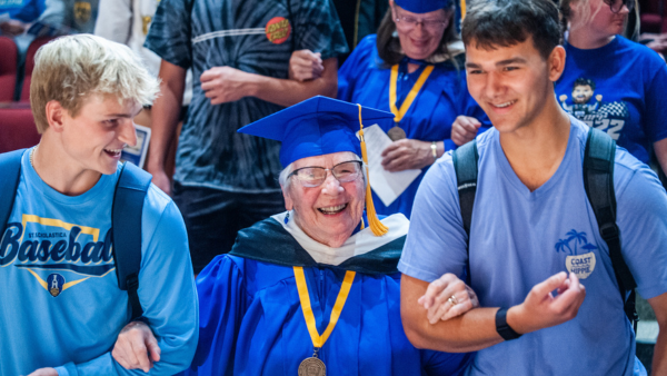 Two students assist an alum down the stairs of Mitchell Auditorium.